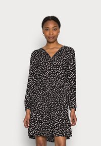 Vestido preto com mangas longas, decote em V e design em camadas, decorado com um padrão de folhas brancas sobre um fundo preto. Textura de tecido suave.