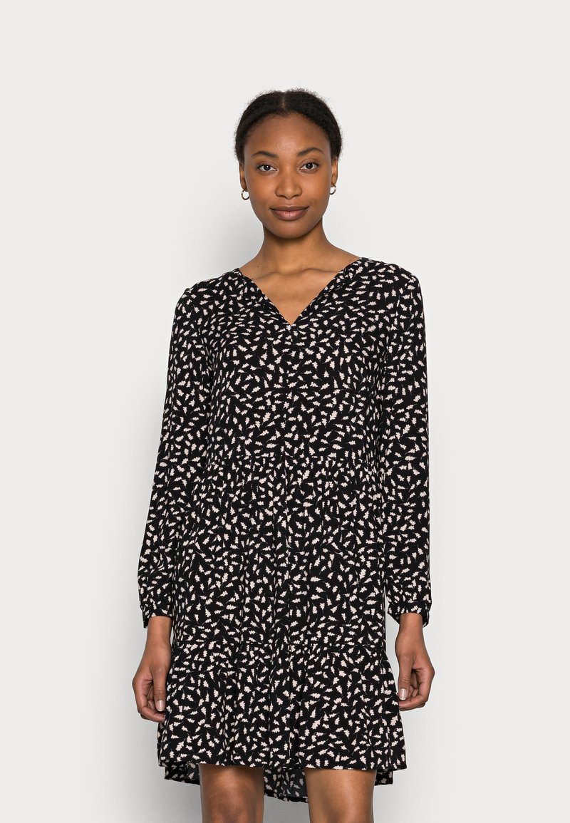 Vestido preto com mangas longas, decote em V e design em camadas, decorado com um padrão de folhas brancas sobre um fundo preto. Textura de tecido suave.