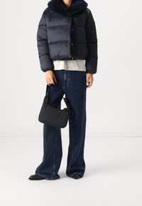 Mörkblå vadderad jacka med pälskrage, grå sweatshirt under, vida mörka jeans, svart axelremsväska och svarta slip-on skor.