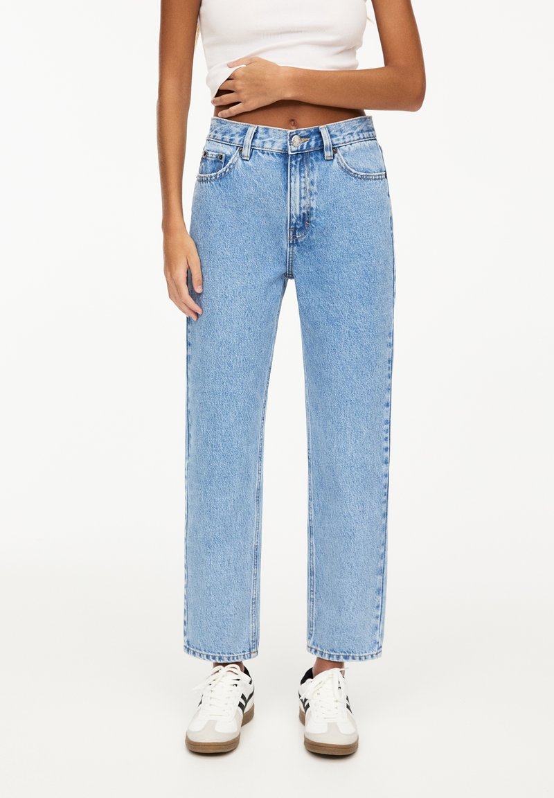 Jean en denim bleu clair avec une coupe ample, taille haute, cinq poches et une jambe droite, associés à des baskets blanches.