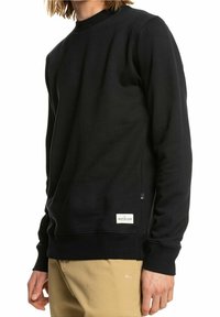 Felpa nera in misto cotone, con scollo rotondo, maniche lunghe, polsini a costine e etichetta con il logo Quiksilver all'orlo.