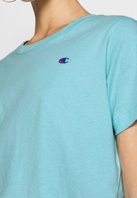 Primer plano de una persona que lleva una camiseta Champion de color azul claro con un pequeño logo bordado de Champion en el pecho.