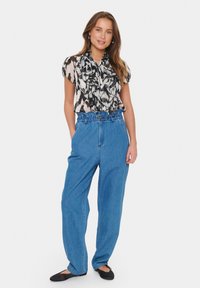 Black and white ruffled blouse paired with blue high-waisted denim pants and black flats. Blouse features a soft, flowing fabric.
