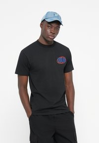 Sort bomulds T-shirt med korte ærmer og rund halsudskæring, der har et rødt og blåt broderet "HUF" logo på brystet.