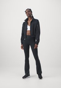Black cropped athletic jacket with zip closure, elastic waistband, paired with high-waisted black leggings and black athletic shoes.