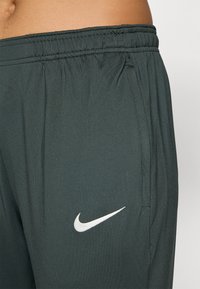 Nike sportshorts i mørkegrønn stoff. Har en elastisk linning og en hvit Nike-logo på venstre side. Glatt tekstur.