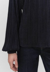 Mørkeblå ribbet langærmet top med en puffet ærmedesign. Stoffet ser tekstureret ud, parret med mørke jeans i lige ben skæring.