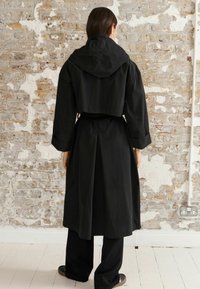 Svart trenchcoat med stor huva, knytdesign i midjan och vida ärmar, med en elegant design och slät yta.