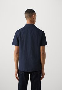 La shirt navy a maniche corte con una finitura testurizzata e un colletto classico. La camicia ha un taglio dritto con un orlo arrotondato.