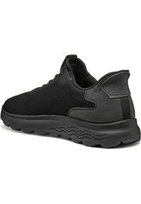 Zapatilla negra con parte superior de malla y suela de goma, que presenta un diseño texturizado, cuello acolchado y logo en relieve en el talón.