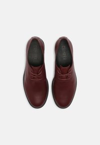 Paire de chaussures en cuir rouge foncé à lacets avec semelles noires, vues de dessus sur un fond blanc uni.