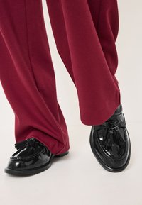 Sorte patentloafere med dusker, med en glatt tekstur og rund tå, kombinert med brede burgunderbukser laget av ribbet stoff.