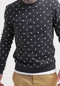 Sudadera negra con estampados geométricos y tropicales en blanco, incluyendo gafas de sol, lunas y triángulos; puños y dobladillo acanalados.