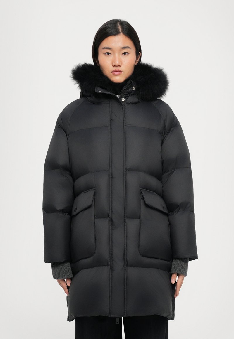 Black puffer coat featuring a plush fur-lined hood, side pockets, and a quilted design. Made of a glossy, insulated material.