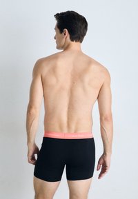 Zwarte boxershorts met een roze Calvin Klein tailleband. Het model is van achteren getoond, waardoor een gladde rug- en armtextuur zichtbaar is.