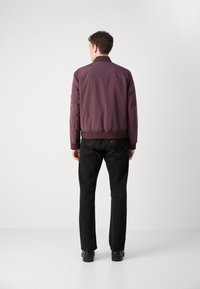 Maroon bomber jacket with a ribbed collar, side pockets, and elastic waistband, paired with black straight-leg jeans and black shoes.