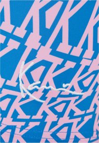 Modrá látka s abstraktným ružovým vzorom a štylizovanými písmenami. V popredí je viditeľný biely vyšitý podpis.