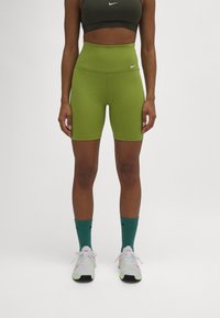 Pantalones cortos verdes de talle alto de Nike, hechos de un material elástico, con una textura suave y un logotipo sutil. Combinados con zapatillas blancas y verdes.