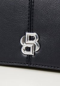 Borsa a tracolla in pelle blu navy con logo intrecciato argentato e accenti di cucitura a contrasto. Texture liscia con un design strutturato.