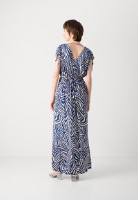 Robe maxi à motif zigzag bleu et beige, dotée d'un dos en V, de manches courtes avec liens, et d'une taille élastique pour une silhouette ajustée.