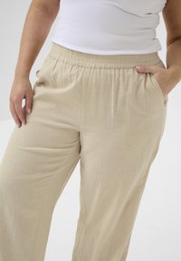 Pantaloni leggeri beige realizzati in tessuto morbido con una finitura testurizzata. Presentano una vita elastica e tasche laterali per una maggiore comodità.