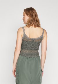 Grå blondetopp med tynne stropper, med blomstermønster og tettsittende design, sammen med et olivengrønt skjørt.