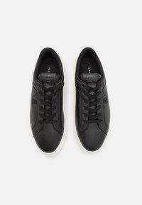 Baskets en cuir noir avec une texture lisse, un design à lacets, une semelle extérieure blanche contrastante et un détail de logo embossé sur le dessus.