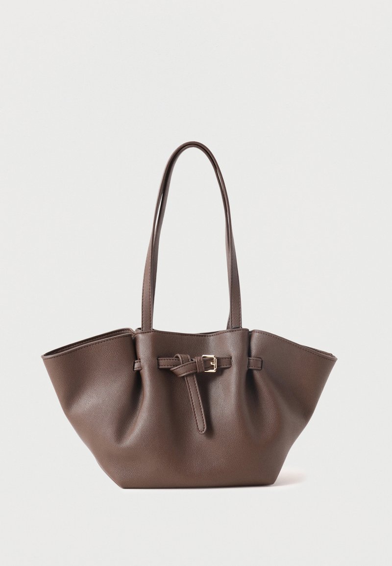 Καφέ δερμάτινη τσάντα ώμου με μακριές λαβές και διακοσμητικό λουράκι με πόρπη στο μπροστινό μέρος, παρουσιάζεται πάνω σε λευκό απλό φόντο.