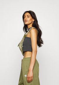 Szary crop top z dekoltem w serek oraz oliwkowe spodnie cargo. Strój zawiera kontrastowy pasek z logiem umieszczony na ramieniu.