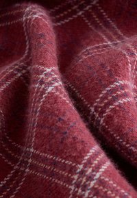 Wollstoff in tiefem Rot mit einem Karomuster. Auffällige Details sind weiße und blaue Akzente, weiche Textur und ein leicht flauschiges Finish.