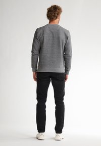 Grijze crewneck sweatshirt van fleece materiaal, met ribbelboorden en zoom, gecombineerd met zwarte slim-fit jeans en witte sneakers.