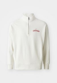 Sudadera de pullover en crema claro con cuello alto, cierre de media cremallera y logo bordado en rojo "calvin" en el pecho. Textura suave, corte relajado.