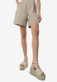 Beige wedge sandalen met een geweven textuur platform, een gladde bovenkant en een enkelbandje. De zool is iets donkerder dan het bovenmateriaal.