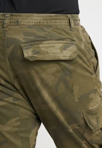 Cargo bukser i en olivengrøn camouflage mønster, med en lomme på bagsiden og et let struktureret stof.