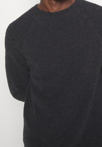 Schwarzer, flauschiger Pullover mit rundem Ausschnitt und langen Ärmeln. Der Stoff hat eine weiche Textur und zeigt ein dezentes, einheitliches Finish.
