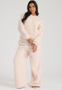 Light pink fleece loungewear set with a textured finish, featuring a loose-fit sweatshirt and wide-leg pants. Soft and cozy fabric.