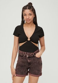 Czarny, prążkowany body z głębokim dekoltem i centralnym wycięciem, w zestawie z różowymi szortami dżinsowymi o podwyższonym stanie i podwiniętych nogawkach.