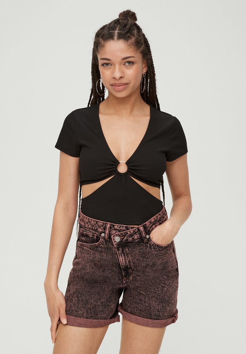 Czarny, prążkowany body z głębokim dekoltem i centralnym wycięciem, w zestawie z różowymi szortami dżinsowymi o podwyższonym stanie i podwiniętych nogawkach.