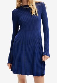 Vestito a maglia a coste in un blu vivace, con maniche lunghe, scollatura rotonda e orlo svasato con un leggero taglio asimmetrico.