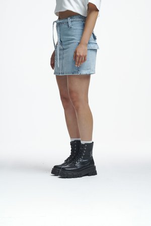 Απαλή μπλε τζιν φούστα με ζώνη που δένει, πλαϊνές τσέπες και φθαρμένο τελείωμα, συνδυασμένη με μαύρες μποτάκια μέχρι το γόνατο με κορδόνια και παχιές σόλες.