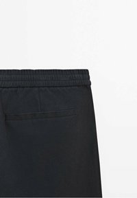 Zwarte broek met een elastische tailleband, een vlakke achterzak en een gladde, duurzame stof met een subtiele textuur.