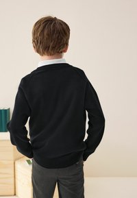 Black knit sweater with a crew neckline, ribbed cuffs, and hem, worn over a white collared shirt; gray trousers visible at the waist.