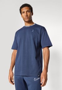 Marineblå t-shirt lavet af bomuld; har en rund halsudskæring med "JUST DO IT" tekst, et struktureret logo på brystet og et lille mærkede tag i kanten.