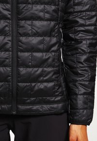 Schwarze gesteppte Jacke mit einer glatten, glänzenden Textur. Verfügt über einen zentralen Reißverschluss und elastische Bündchen. Leicht und tailliert im Design.