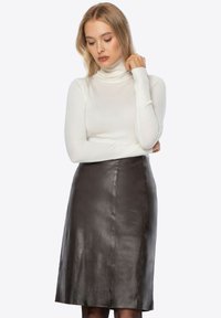 Ciemnobrązowa skórzana spódnica ołówkowa o gładkiej fakturze, zestawiona z dopasowanym białym golfem. Spódnica sięga do połowy łydki.