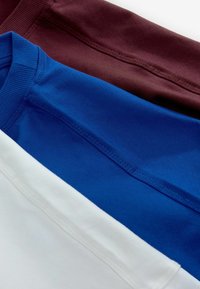 Trzy koszulki ułożone jedna na drugiej: burgundowa, królewsko niebieska i biała. Bawełnowy materiał, krótkie rękawy, prążkowane dekolty, gładka tekstura.