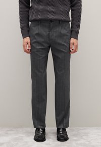 Graue gestreifte Stoffhose mit glatter Struktur, geradem Schnitt und Vordertaschen, kombiniert mit schwarzen Schuhen.