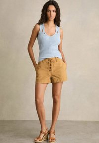 Lyseblå ribbet tanktop med udskæringer, parret med brune højtaljede shorts med snøredetaljer foran, og brune kile-sandaler.