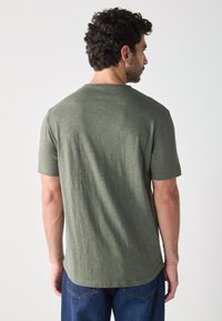 Olijfgroen T-shirt met korte mouwen en een ronde hals, met een zachte textuur en een iets gebogen zoom, gecombineerd met blauwe spijkerbroeken.