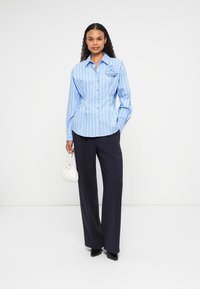 Light blue striped button-up shirt with a floral accent on the left chest, paired with dark wide-leg trousers and a white bag.